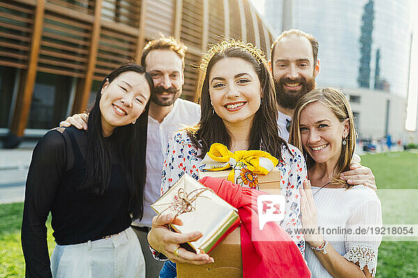 Happy woman holding gifts with friends in park