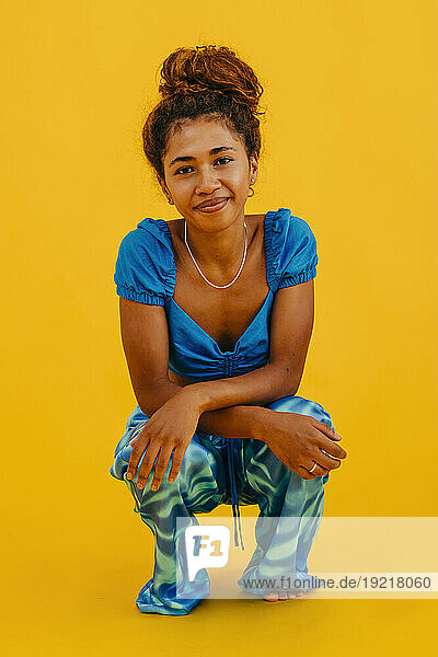 Smiling woman wearing casual crouching against yellow background