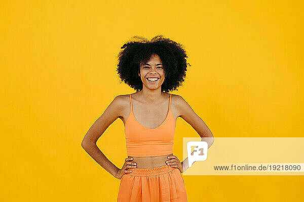 Happy woman standing with arms akimbo against yellow background