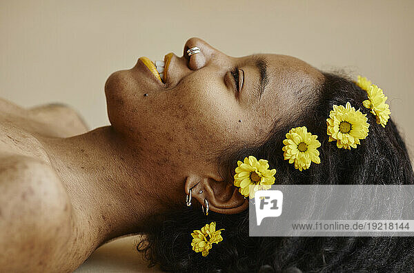 Woman with yellow flowers on hair against brown background