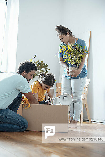 Mother holding plant with father and daughter packing lamp in box