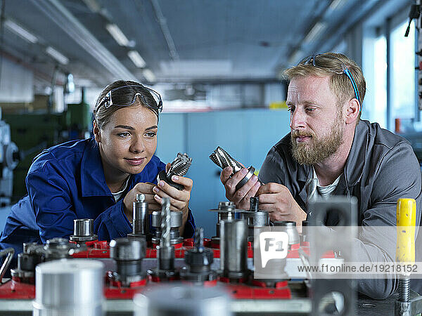 Trainee with metal worker examining CNC tools in factory