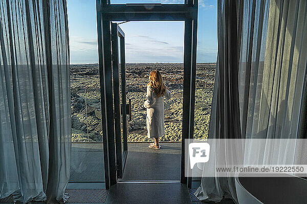 Woman standing on balcony in a bathrobe overlooking the lava fields in Southern Iceland; Blue Lagoon  South Iceland  Iceland