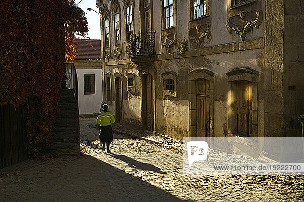 Backlit view of a woman walking down a cobbled street in a village; Provesende  Douro River Valley  Portugal