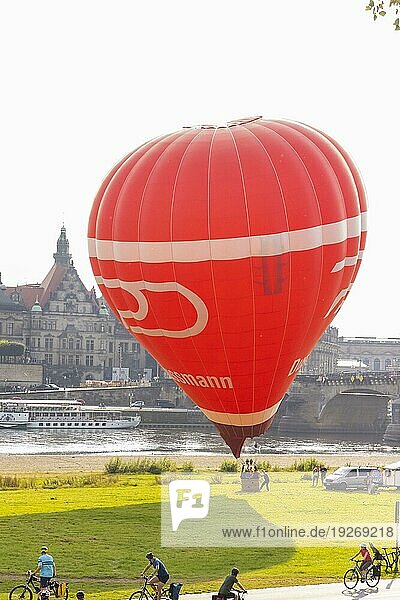 Ein roter Heißluftballon startet am Königsufer  gegenüber der historischen Silhouette der Dresdner Altstadt an der Elbe