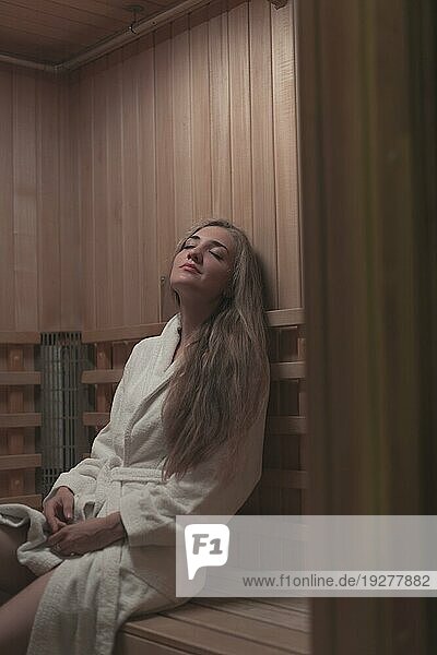 Frau weißer Bademantel sitzend Holzbank entspannende Sauna