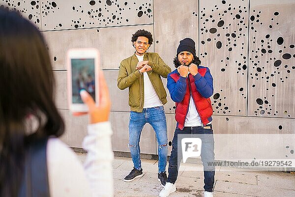 Urbaner Stil  zwei Jungs  die ein Video für soziale Netzwerke aufnehmen  zwei schwarze Latino Freunde  die Spaß auf der Straße haben. Afro Haar Junge  Brünette Junge mit langen Haaren mit Hut