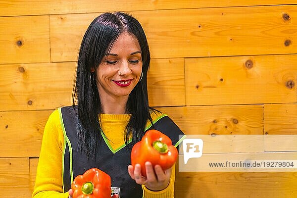 Ein brünettes kaukasisches Obstmädchen  das in einem Gemüseladen arbeitet  hat Spaß an roten Paprika in der Hand