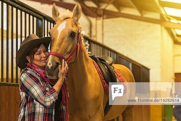 Porträt einer erwachsenen Frau in einem Pferdestall  die ein braunes Pferd streichelt  gekleidet in südamerikanische Tracht