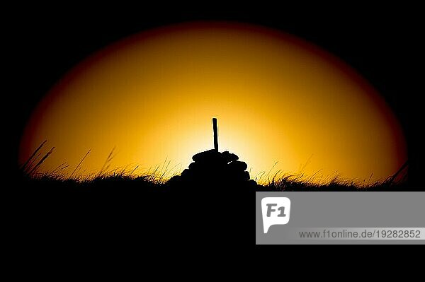 Silhouette eines Steinhaufens mit einem Stock bei Sonnenaufgang im Kreis