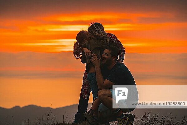 Eine Familie  die sich auf dem Gipfel eines Berges bei Sonnenuntergang umarmt und Spaß hat. Abenteuer Lebensstil Ein Sommernachmittag in den Bergen des Baskenlandes