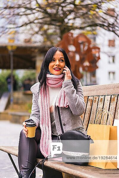 Lifestyle  ein kaukasisches brünettes Mädchen  das mit Papiertüten und einem Kaffee zum Mitnehmen in der Stadt einkauft und sich auf einen Anruf setzt