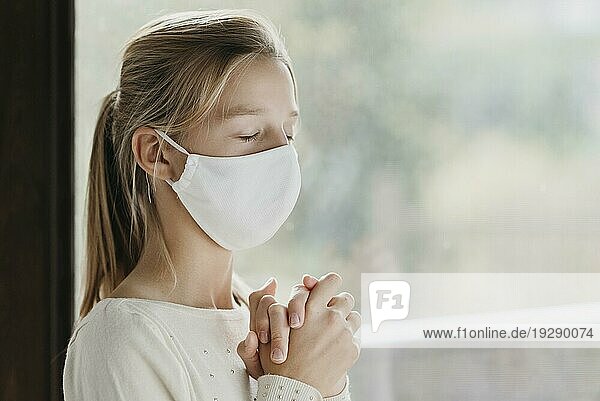 Kleines Mädchen mit medizinischer Maske beim Beten