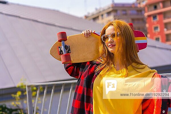 Skateboardfahrerin in gelbem Hemd  rotkariertem Hemd und Sonnenbrille  in einer Pose mit dem Skateboard nach links