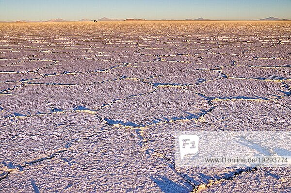 Salar de Uyuni: Der Sonnenaufgang am Salzsee erzeugt ein schönes Muster. In der Ferne fährt ein Jeep über den Salzsee