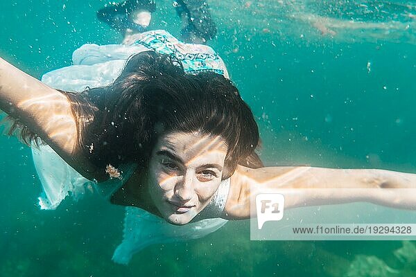 Eine junge Frau taucht mit einem weißen Kleid schwimmen  Unterwasserbild Sommer Lebensstil eines jungen kaukasischen Brünette Blick auf Kamera