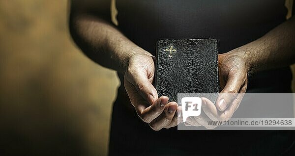 Mann hält eine alte kleine schwarze Bibel in den Händen. Kurze Schärfentiefe  die Schärfe liegt im Kreuz