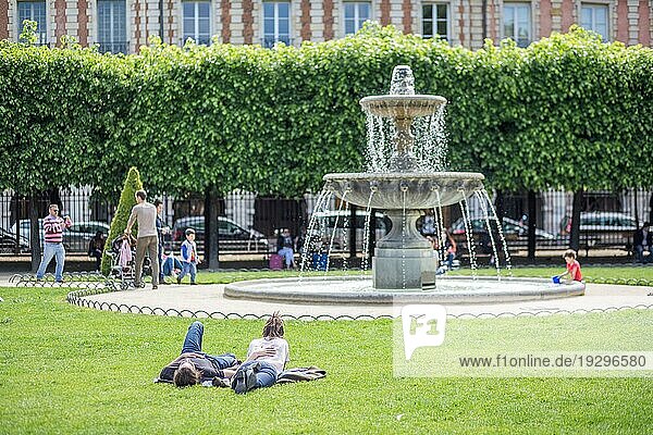 Paris  Frankreich  13. Mai 2017: Ein junges Paar liegt vor einem Springbrunnen auf dem Place des Vosges  Europa