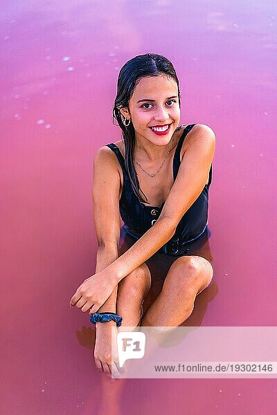 Posing einer jungen brünetten Kaukasierin im Sommerurlaub in der rosa Lagune von Torrevieja  die lächelnd im Wasser sitzt  Alicante. Spanien