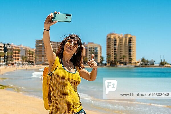 Eine sehr glückliche junge Frau macht ein Selfie mit dem Handy in Playa del Cura in der Küstenstadt Torrevieja  Alicante  Valencianische Gemeinschaft. Spanien  Mittelmeer