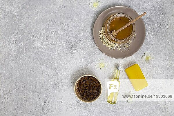 Erhöhte Ansicht Honig gelbe Seife ätherisches Öl Flasche Kaffeepulver mit weißen Blumen Betonhintergrund