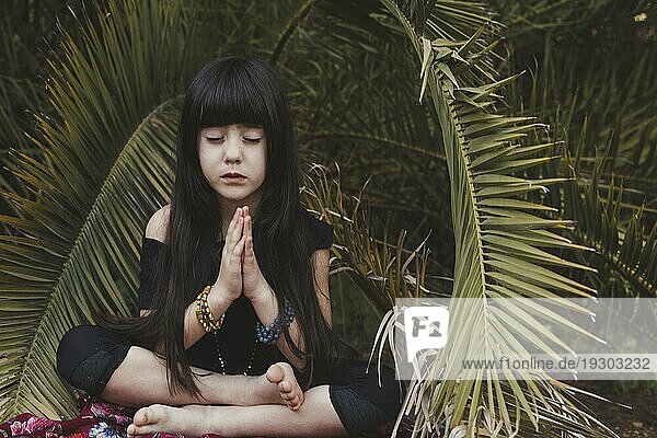 Süßes Mädchen meditiert in der Nähe von Palmen