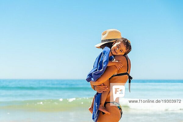Mutter mit Hut  die ihren Sohn umarmt und sich mit ihm am Meer vergnügt  Algarve Strand  Albufeira. Portugal