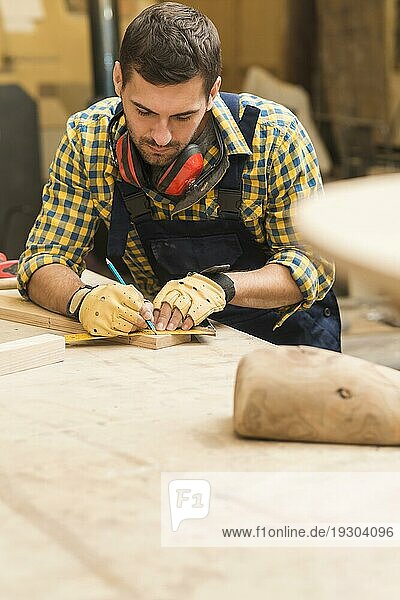 Männlicher Zimmermann  der einen Holzklotz mit Lineal und Bleistift mißt