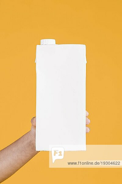 Menschliche Hand hält weißen Milchkasten gelben Hintergrund