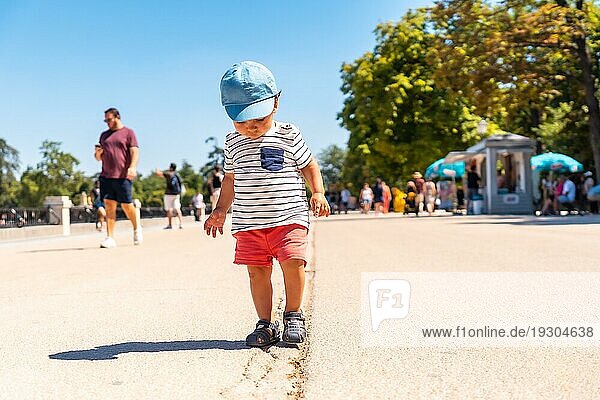 Porträt eines einjährigen kaukasischen Jungen  der mit einer Mütze in einem Park spazieren geht und in die Kamera schaut