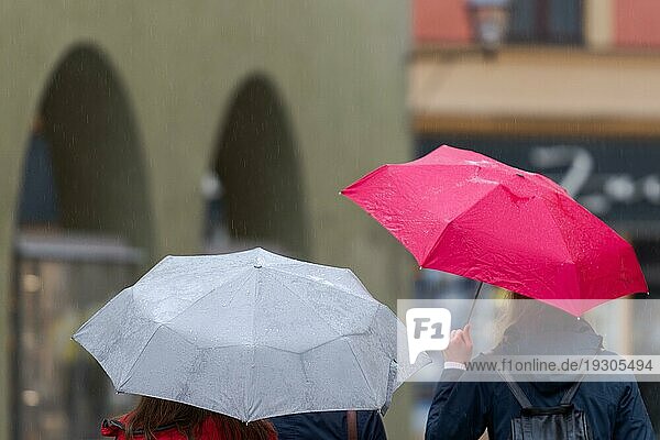 Oberkörperteile von zwei unerkennbaren Menschen mit Regenschirmen  die durch die Straße in einer alten  schmalen Schusterstraße an einem regnerischen Tag gehen