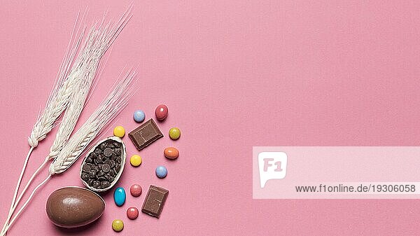 Drei Weizen Ohren mit Schokolade Ostereier Edelstein Bonbons rosa Hintergrund