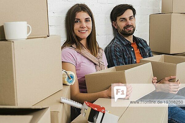 Lächelndes junges Paar hält Kartons und entspannt sich im neuen Haus