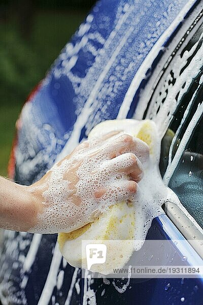 A Hand wäscht ein blaues Auto mit einem Schwamm