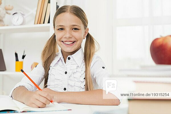Lächelndes blondes Grundschulmädchen bei den Hausaufgaben