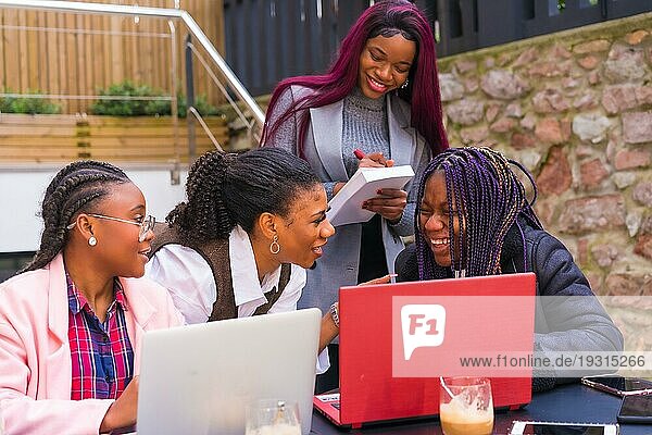 Junge und alternative Geschäftsfrauen schwarzer Ethnie. In einer Teamwork Sitzung  in einer Cafeteria mit Computern und Notizen