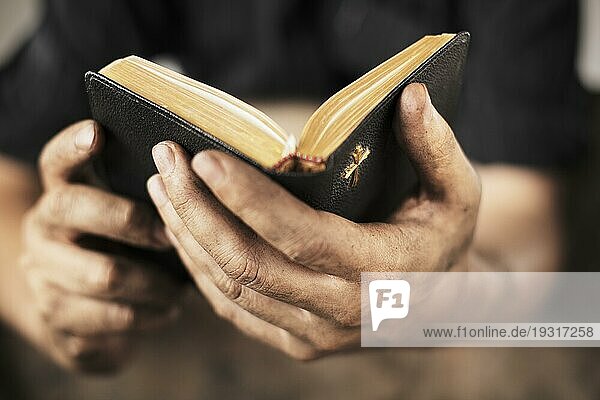 Schmutzige Hände halten eine alte Bibel. Sehr geringe Tiefenschärfe