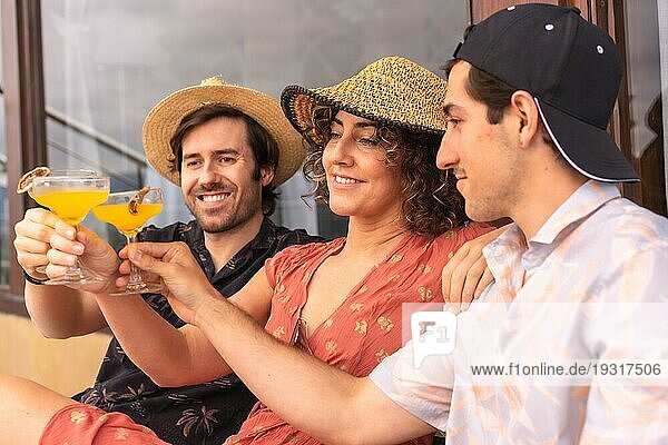 Lässige drei kaukasische Freunde stoßen mit Cocktails entspannt auf einer Terrasse sitzend an