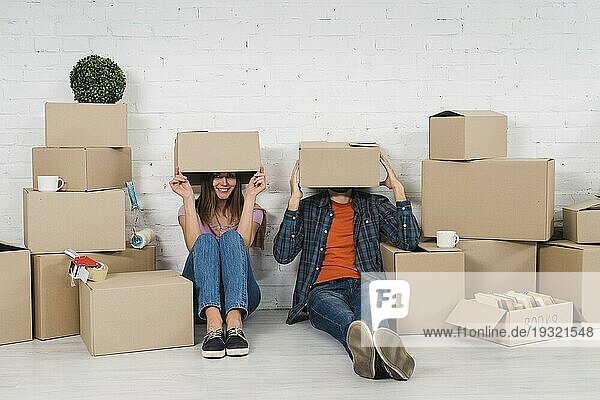 Junges Paar versteckt sein Gesicht und sitzt in Kartons in seinem neuen Haus