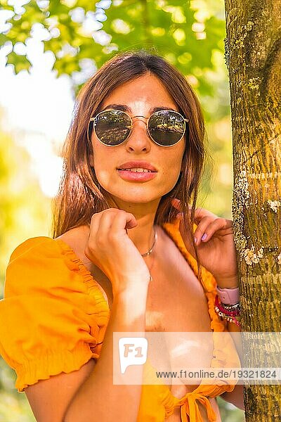 Lifestyle einer jungen kaukasischen jungen Brünette in einem Park im Sommer neben einem Baum in der Natur. Mädchen mit Brille lächelnd  Blick in die Kamera