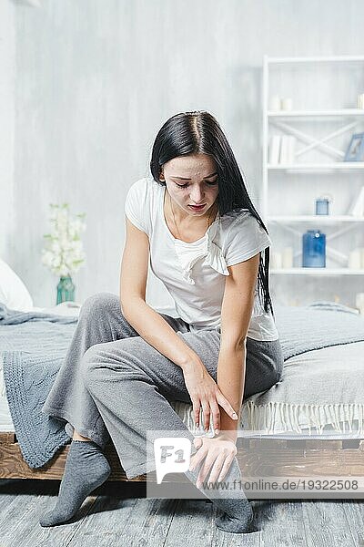 Attraktive junge Frau sitzt im Bett und hat Schmerzen im Knöchel