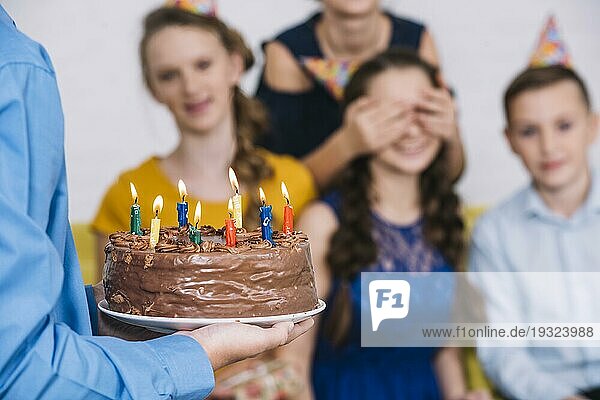 Close up Junge s Hand bringt Schokolade Kuchen Geburtstagskind mit bedeckten Augen von ihrem Freund