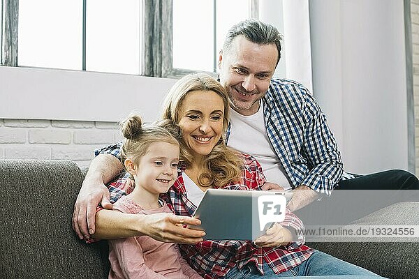 Glückliche Familie auf dem Sofa im Wohnzimmer mit digitalem Tablet