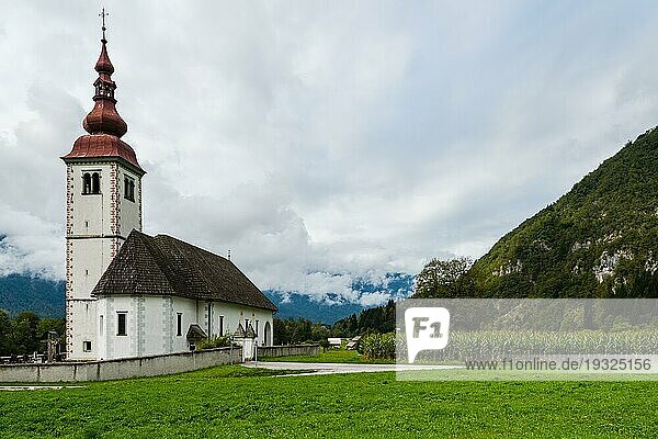 Schöne alte Solitärkirche mit angrenzendem Friedhof in einem Gebirgstal mit frischem Gras und bewölktem Himmel inmitten hoher Berggipfel