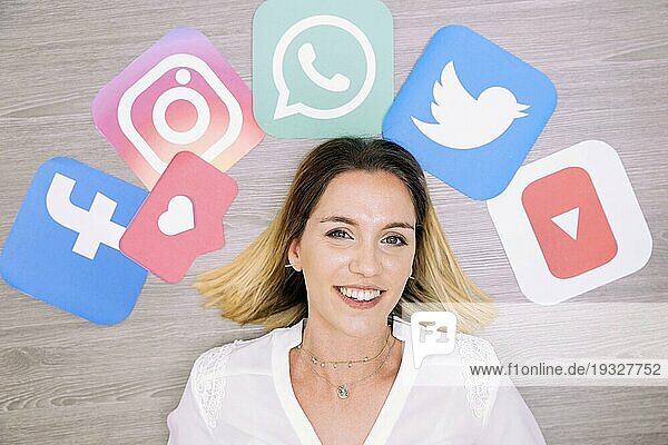 Porträt einer lächelnden Frau  die vor einer Wand mit Symbolen für soziale Netzwerke steht