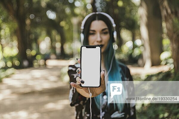 Porträt einer jungen Frau  die ein leeres weißes Smartphone zeigt