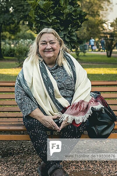 Porträt einer fröhlichen älteren Frau  die auf einer Bank in einem öffentlichen Park sitzt und sich im Freien entspannt