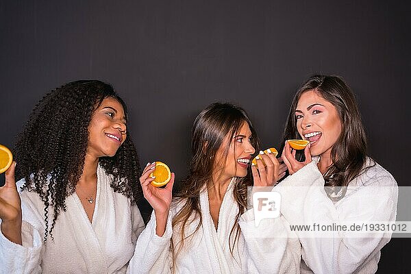 Studiofoto mit grauem Hintergrund von multiethnischen entspannten Frauen im Bademantel  die Obst essen