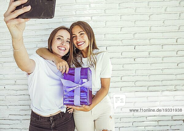 Zwei lächelnde Freundinnen mit Geschenk nehmen Selfie Smartphone