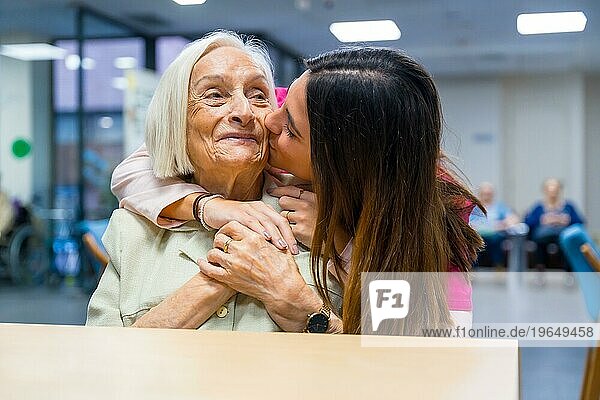 Krankenschwester küsst und umarmt von hinten eine süße ältere Frau in einer geriatrischen